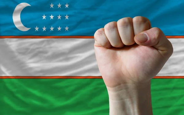 Жесткий кулак перед флагом Узбекистана, символизирующим власть — стоковое фото