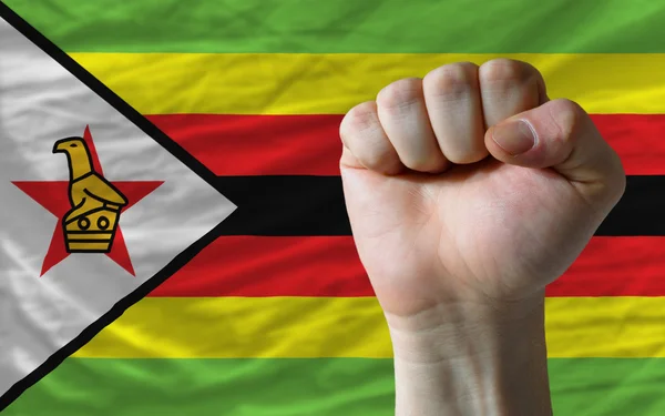 Puño duro frente a la bandera de zimbabwe que simboliza el poder — Foto de Stock