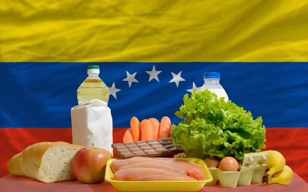 Abarrotes de alimentos básicos frente a la bandera nacional de venezuela — Foto de Stock
