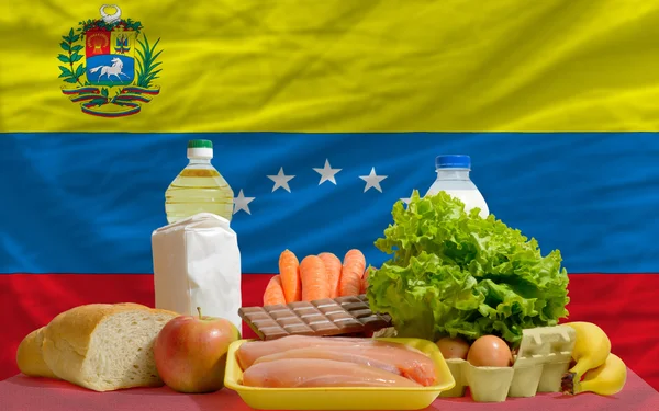 Abarrotes de alimentos básicos frente a la bandera nacional de venezuela — Foto de Stock