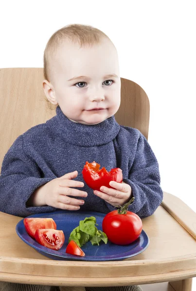 Маленький ребенок ест помидоры в стульчике — стоковое фото