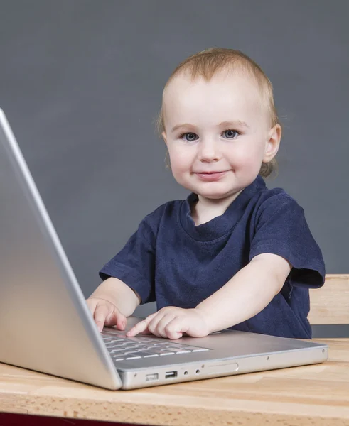 Bebê com computador portátil em fundo cinza — Fotografia de Stock