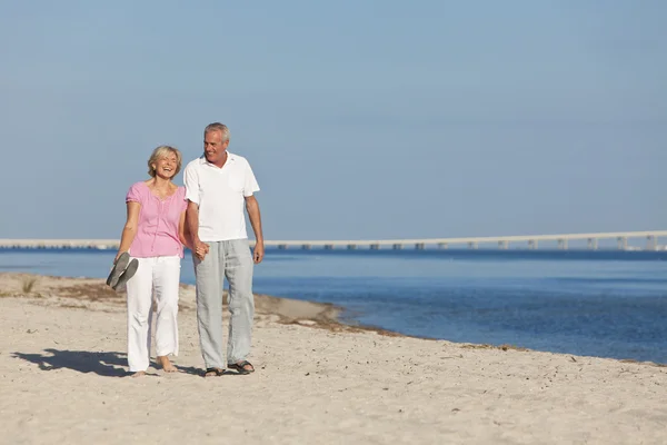 Счастливая пожилая пара гуляет, держась за руки на пляже — стоковое фото