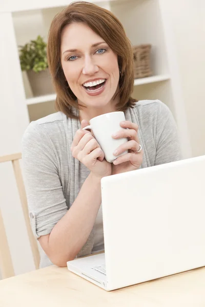 Γυναίκα με φορητό υπολογιστή στο σπίτι πίνει τσάι ή καφέ — Φωτογραφία Αρχείου