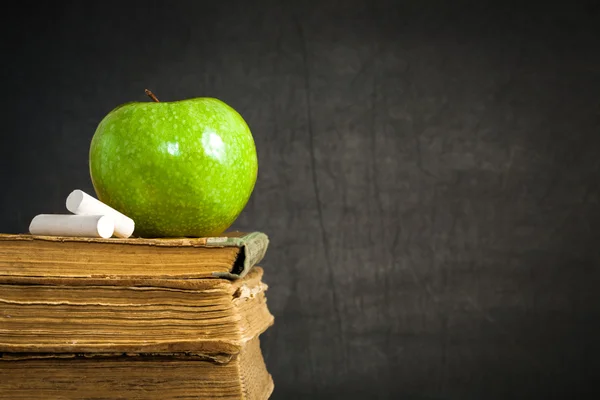 Зеленое яблоко и мел на старых книгах — стоковое фото
