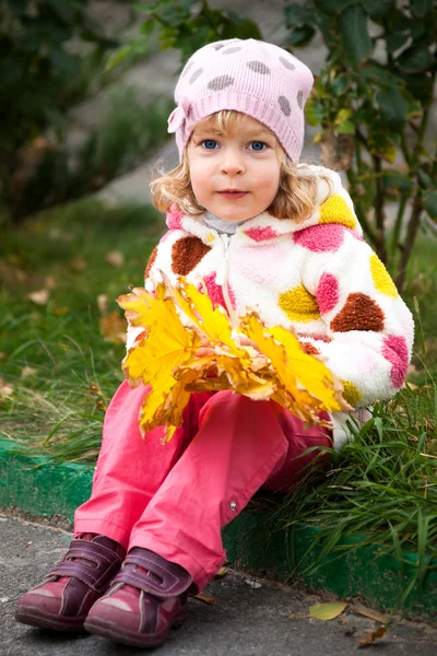 Criança com um monte de folhas amarelas — Fotografia de Stock