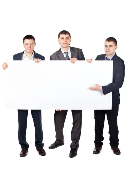 Três jovens empresários seguram um grande sinal em branco isolado em w — Fotografia de Stock