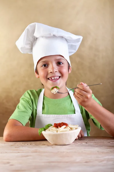 Rapaz feliz com chapéu de chef comer massa — Fotografia de Stock