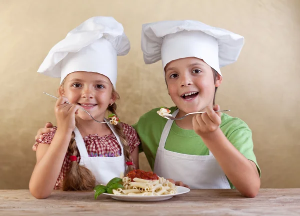 Bambini felici con cappelli da chef che mangiano pasta fresca — Foto Stock