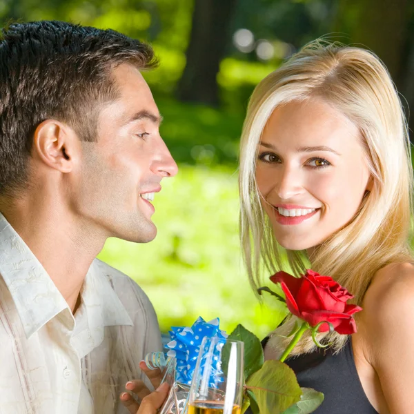 Casal jovem com presentes, rosa e champanhe, ao ar livre — Fotografia de Stock
