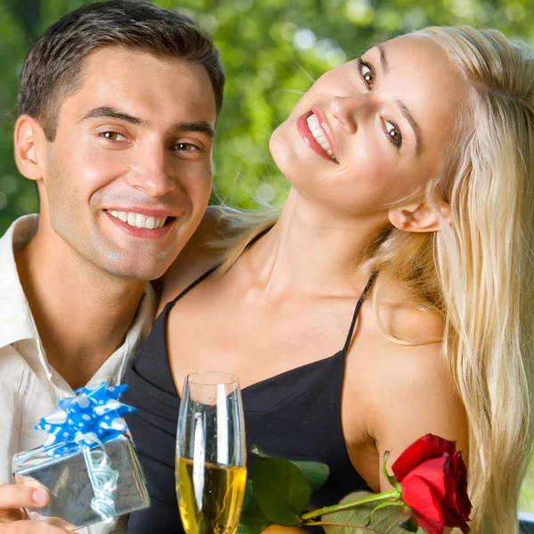 Young couple with gifts, rosa and champagne, outdoor Royalty Free Stock Photos