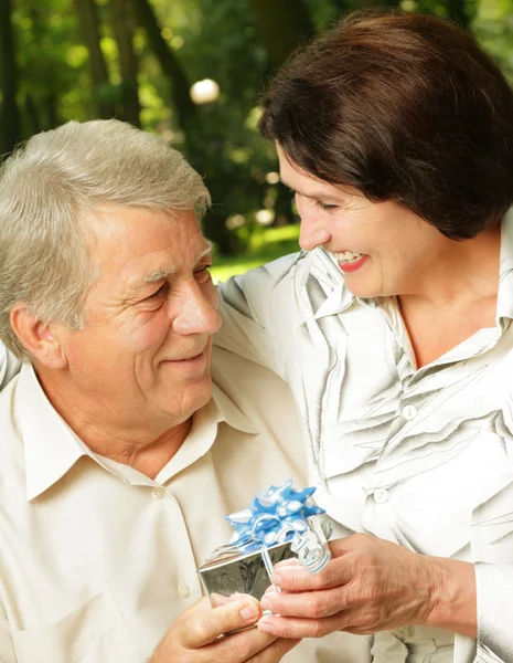 Зрелая счастливая улыбающаяся пара обнимается в парке с подарком — стоковое фото