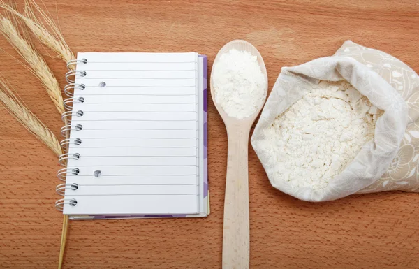 Libro de recetas y harina en un saco con una cuchara sobre una mesa de madera . — Foto de Stock