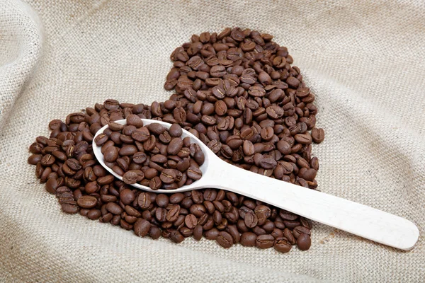 Corazón de los granos de café y cuchara de madera en el saqueo —  Fotos de Stock