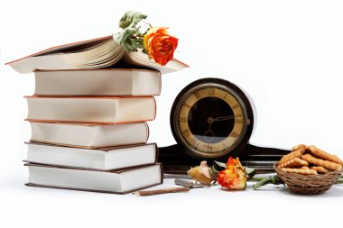 A stack of books and antique clock on a white background. clipart