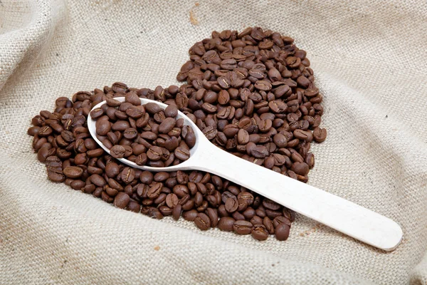 Сердце кофейных зерен и деревянная ложка на мешок — стоковое фото
