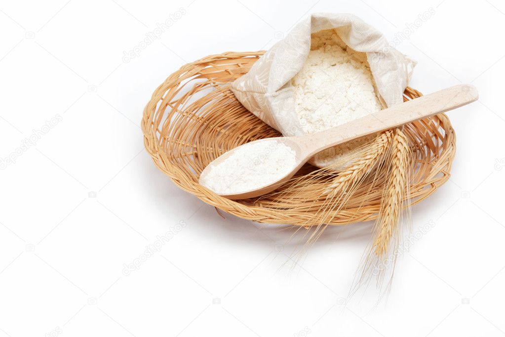 Flour and wheat grain with wooden spoon on a wicker basket.