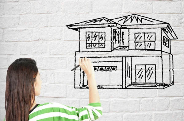 Frau zeichnet Haus auf Ziegelmauer — Stockfoto