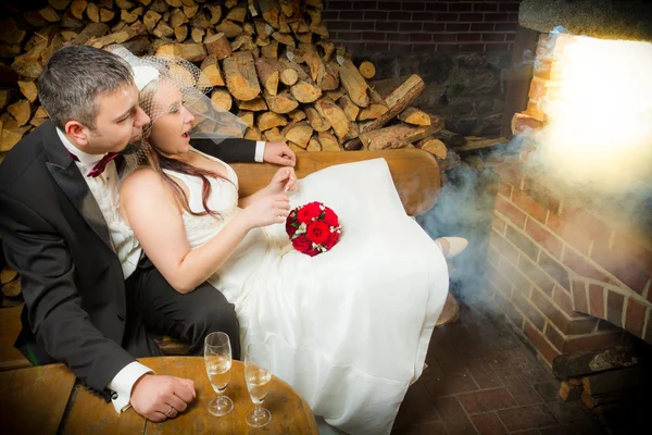 Surprised young couple sitting in front of a smoking fireplace — Stock Photo, Image
