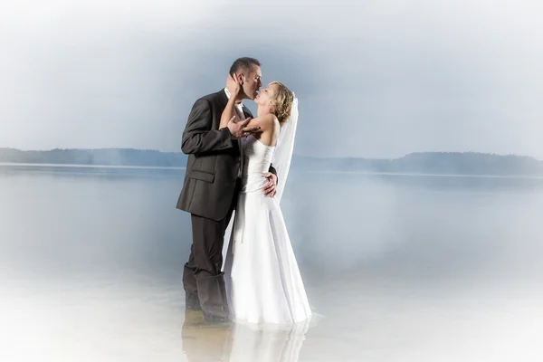 Jovem casal em um lago enevoado em um beijo apaixonado — Fotografia de Stock
