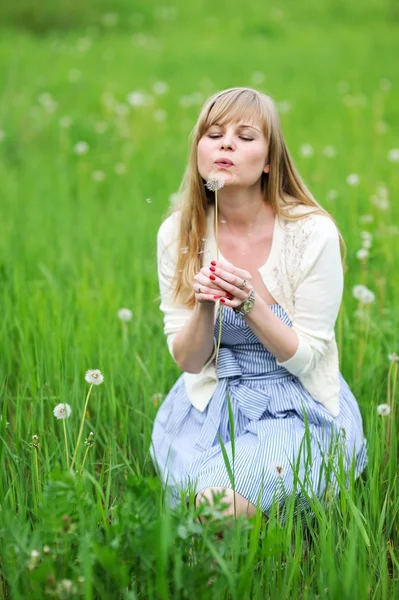 Beautiful young woman blowing away dandelion — Stock Photo, Image