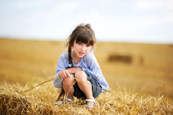 Little girl sitting on a top of haystack — 图库照片