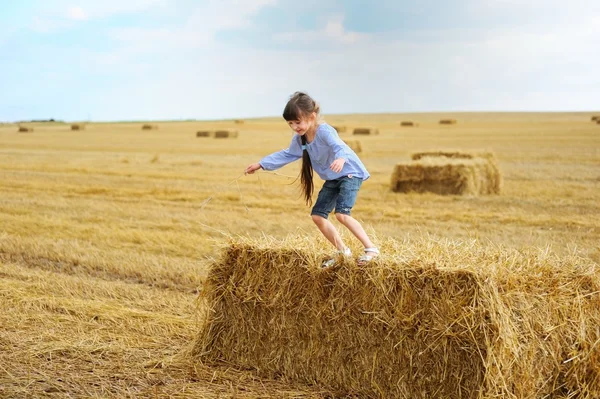 Little girl jumping from a top of haystack — Stock fotografie