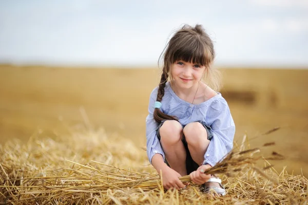 Little girl sitting on a top of haystack — Stock Photo, Image