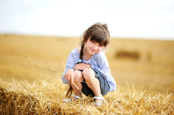Little girl sitting on a top of haystack — 图库照片