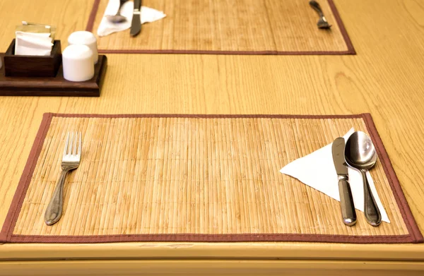 Nomeações de mesa garfo, faca, colher, guardanapo de seda no tapete de bambu — Fotografia de Stock