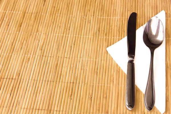 Tischtermine - Gabel, Messer, Löffel, Seidenserviette auf Bambusmatte — Stockfoto
