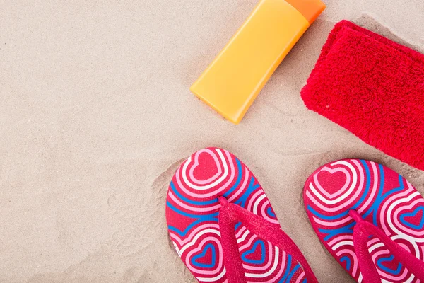Klapki, krem do opalania, ręcznik na piaszczystej plaży — Zdjęcie stockowe