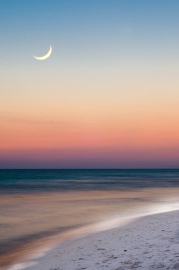 Summer beach scene just after sunset with crescent moon in long exposure image clipart