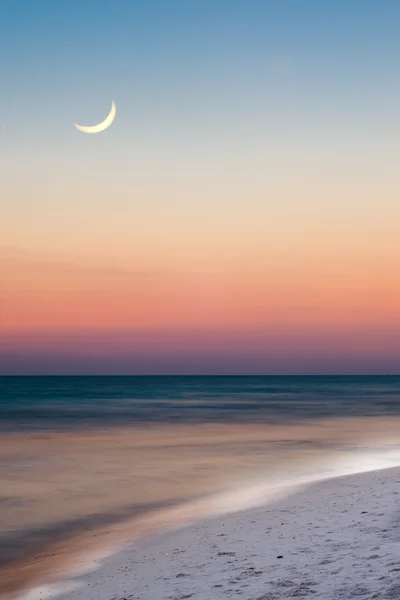 Summer beach scene just after sunset with crescent moon in long exposure image — Stock Photo, Image
