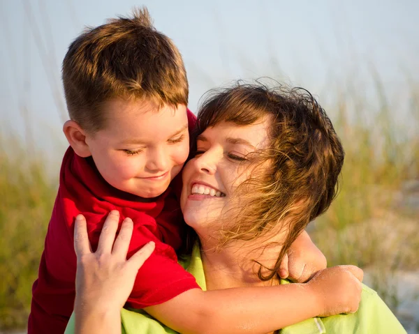 Portrait of happy mother and son hugging at beach with sand dunes in background — Stock Photo, Image
