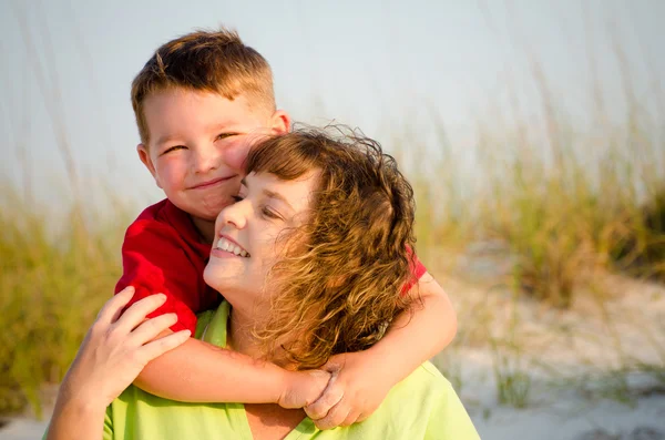 Boldog anya és fia, átölelve a háttérben homokdűnékkel strandon portréja — Stock Fotó
