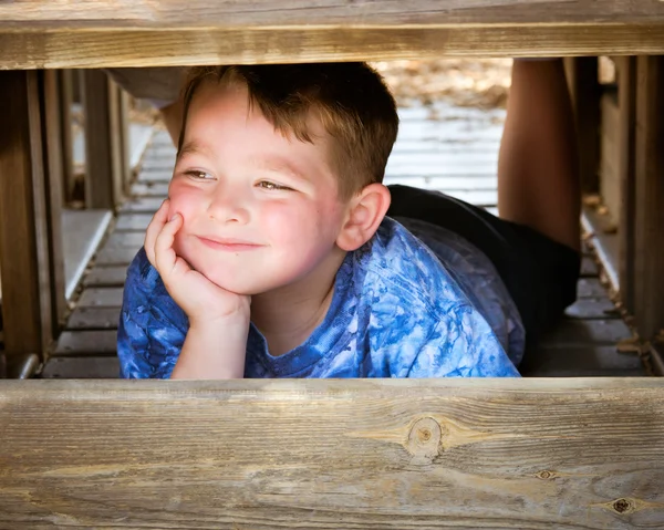 Счастливый улыбчивый мальчик играет и прячется от друзей на детской площадке — стоковое фото