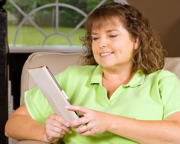 Stock image Woman reading book using an e-reader while relaxing at home