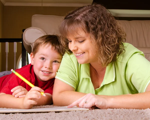 Мать помогает ребенку писать уроки для школы, находясь дома — стоковое фото