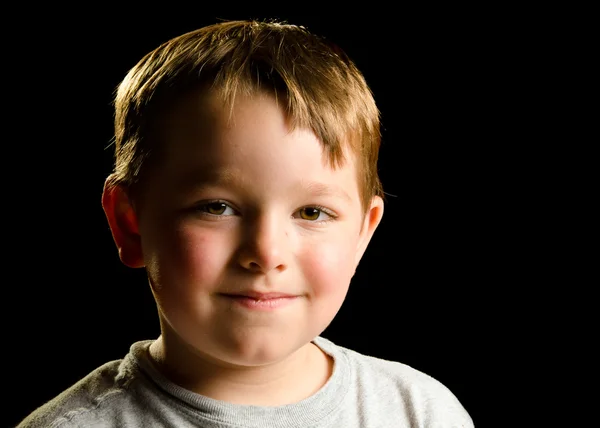 Portrait of mischievous smirking child isolated on black — Stockfoto