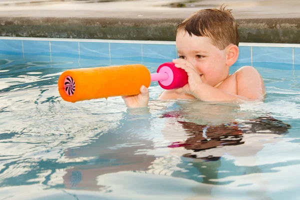 Criança brincando com arma de água enquanto nadava na piscina durante o verão — Fotografia de Stock