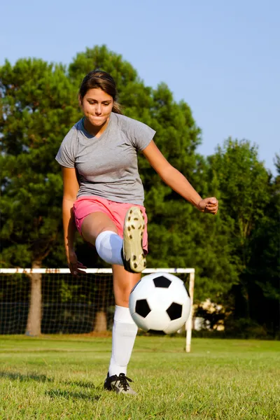 Teen girl kicking soccer ball on field