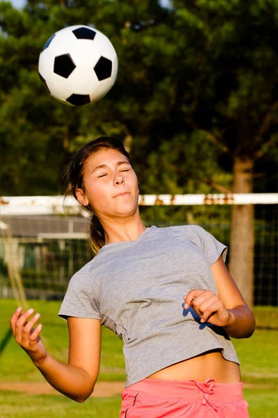 Chica adolescente encabezando pelota de fútbol mientras juega en el campo —  Fotos de Stock