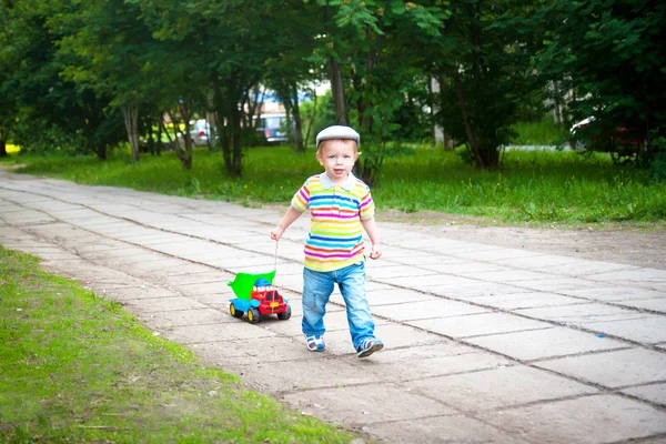 Menino correndo ao longo da estrada com um carro de brinquedo — Fotografia de Stock