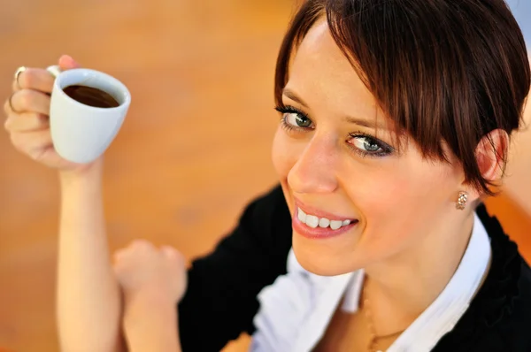 Close-up de morena sorridente segurando uma xícara de café e olhando — Fotografia de Stock