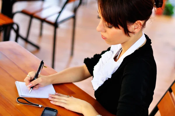 Mujer en la cafetería calculando su presupuesto y escribiendo a bloc de notas —  Fotos de Stock