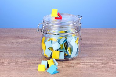 Pieces of paper for lottery in jar on wooden table on blue background clipart