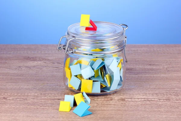Stukjes papier voor loterij in pot op houten tafel op blauwe achtergrond — Stockfoto