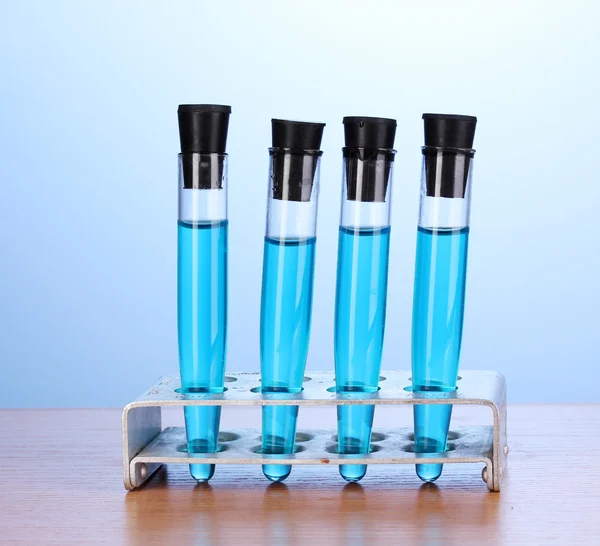 Tubos de ensaio com líquido azul sobre mesa de madeira sobre fundo azul — Fotografia de Stock