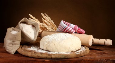 Dough and bags with flour on wooden table on brown background clipart